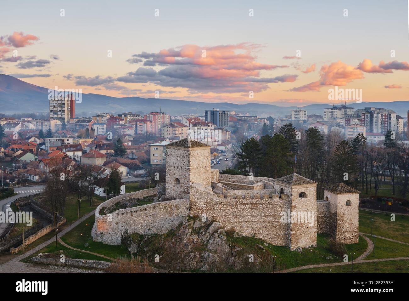 Wunderschöne, sanfte Farben der Wolken auf einem Sonnenuntergangshimmel über der alten Festung vor einer landschaftlich schönen, nebligen, verträumten Stadtlandschaft von Pirot, Serbien Stockfoto