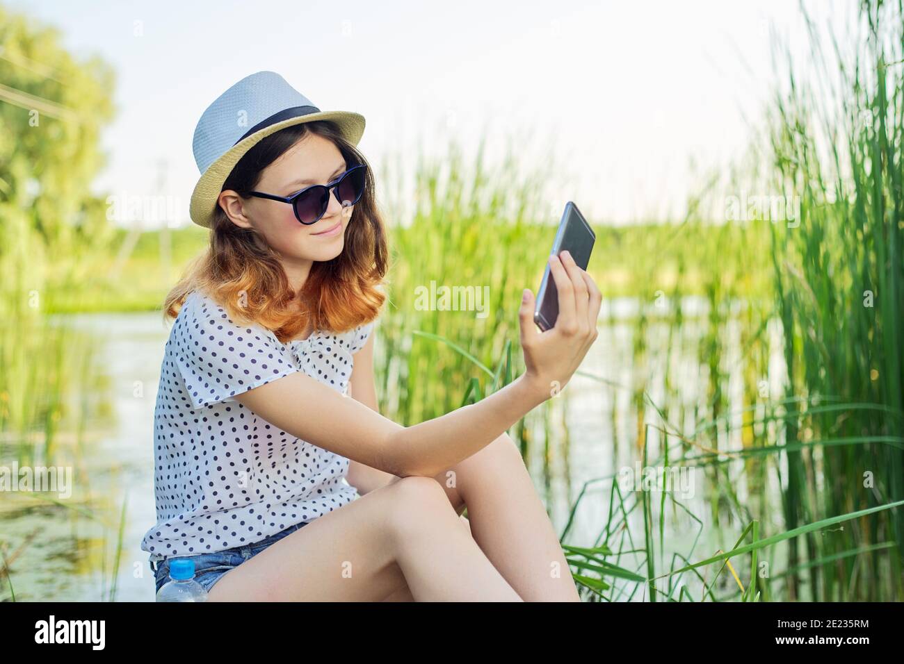 Happy Teenager Mädchen im Hut mit Smartphone auf hölzernen Pier Von See mit Schilf Stockfoto
