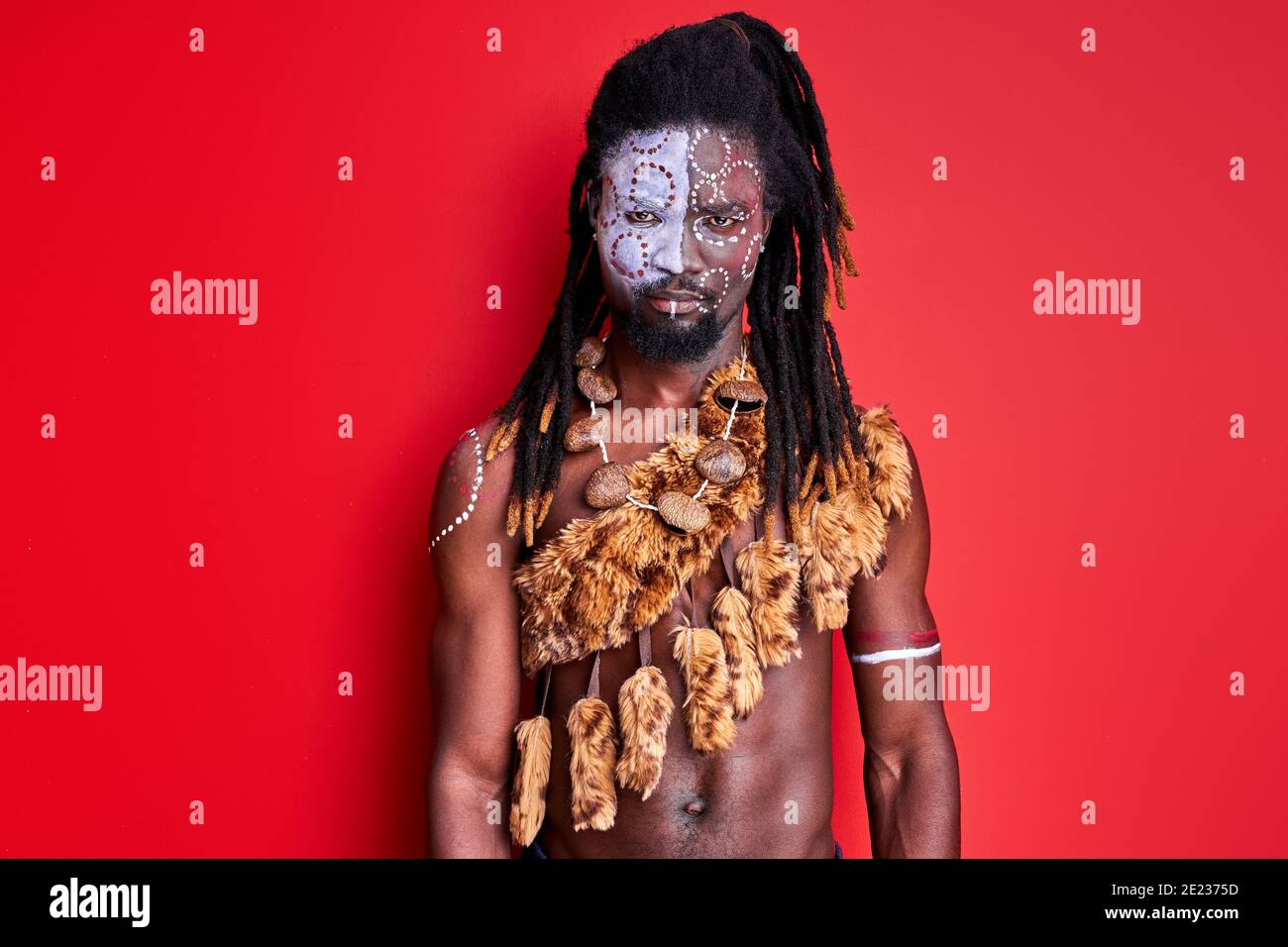 Schwarzer Schamane mit ethnischem Make-up am Körper, im Gesicht. Junger Mann mit Dreadlocks ist selbstbewusst Stockfoto