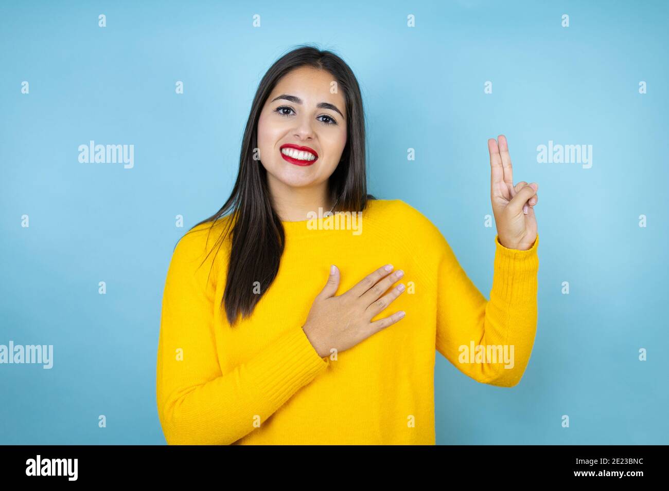 Junge schöne Frau trägt gelben Pullover über isolierten blauen Hintergrund lächelnd Fluchen mit Hand auf Brust und Finger nach oben, so dass eine Loyalität Promis Stockfoto