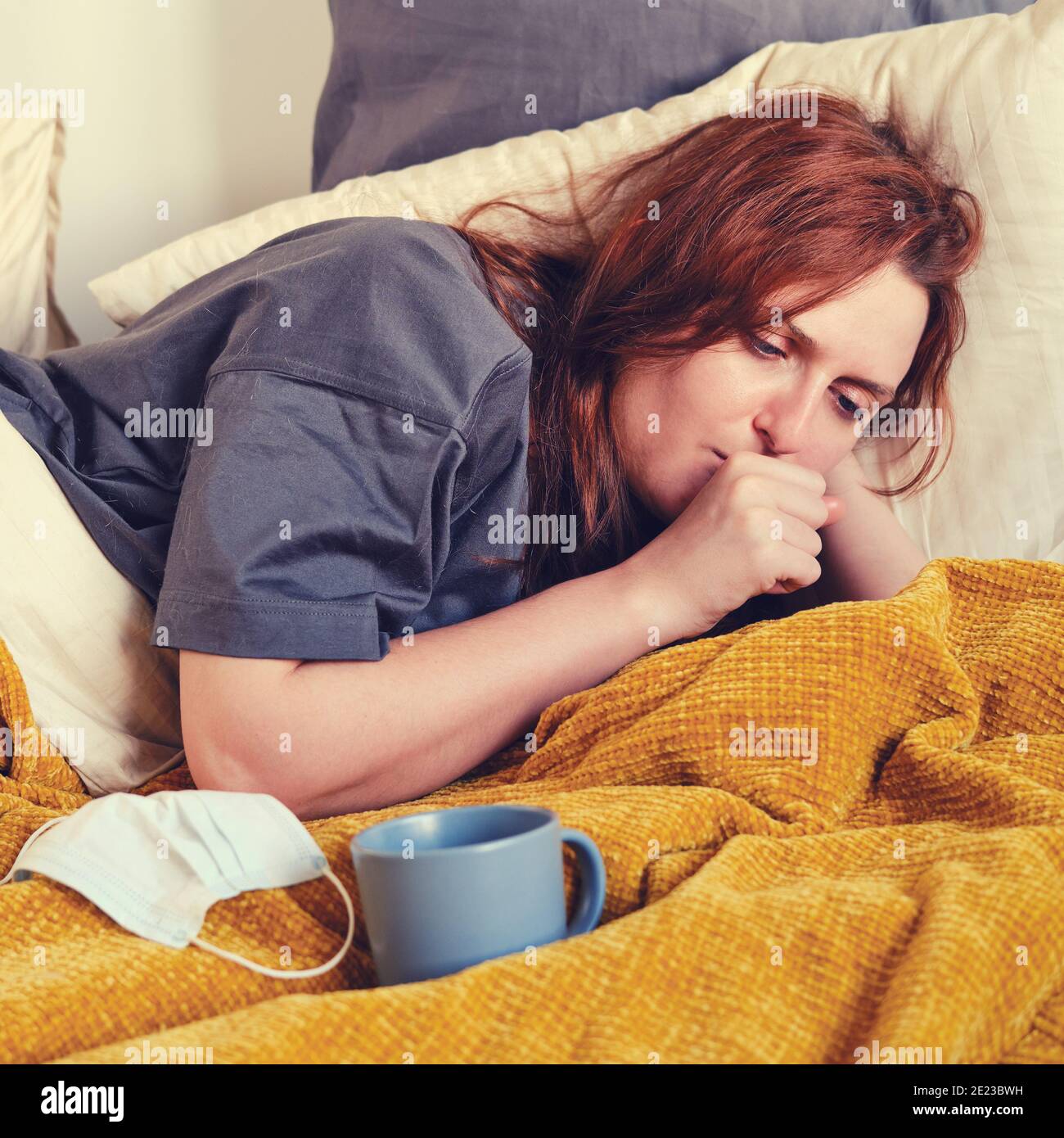 Rotschopf Coronavirus kranke Frau hustet in die Faust, während sie auf liegt Bett zu Hause Stockfoto