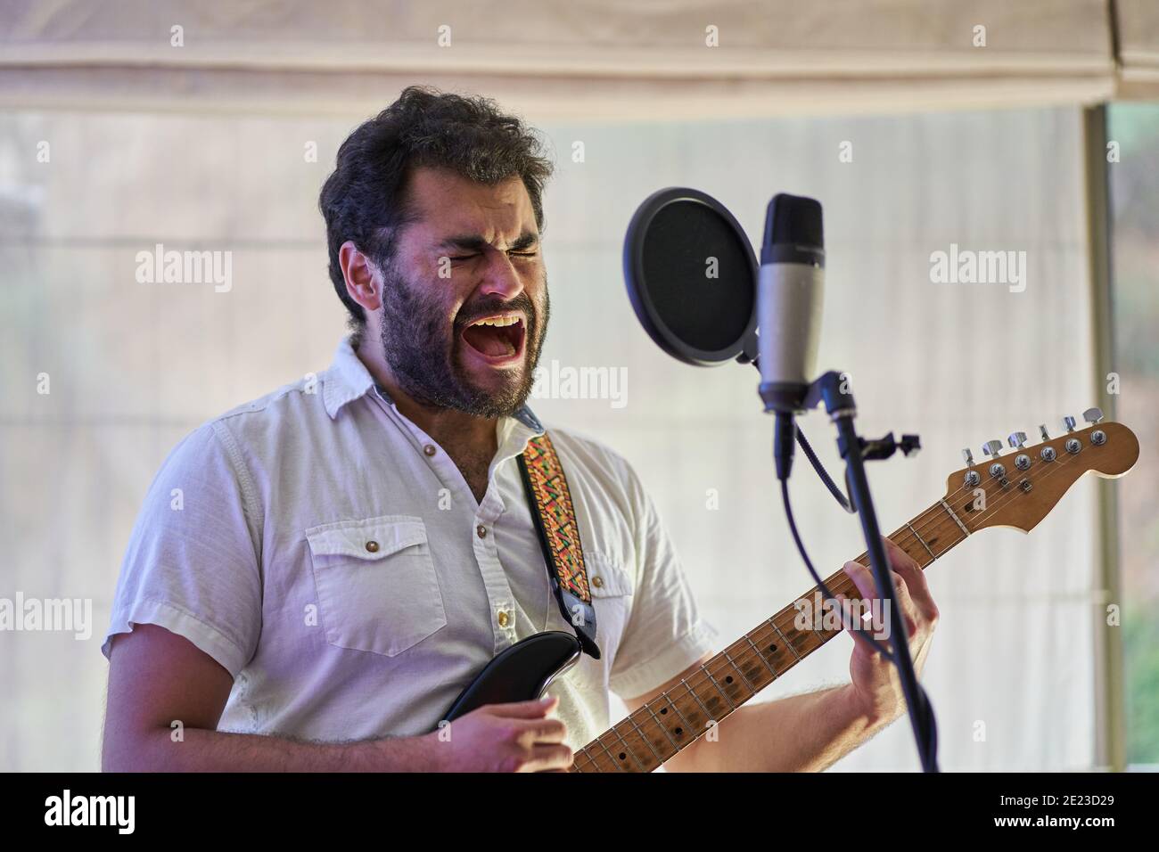 Leidenschaftlicher männlicher Musiker mit E-Gitarre singen begeistert und aufnehmen In einem Studio Stockfoto