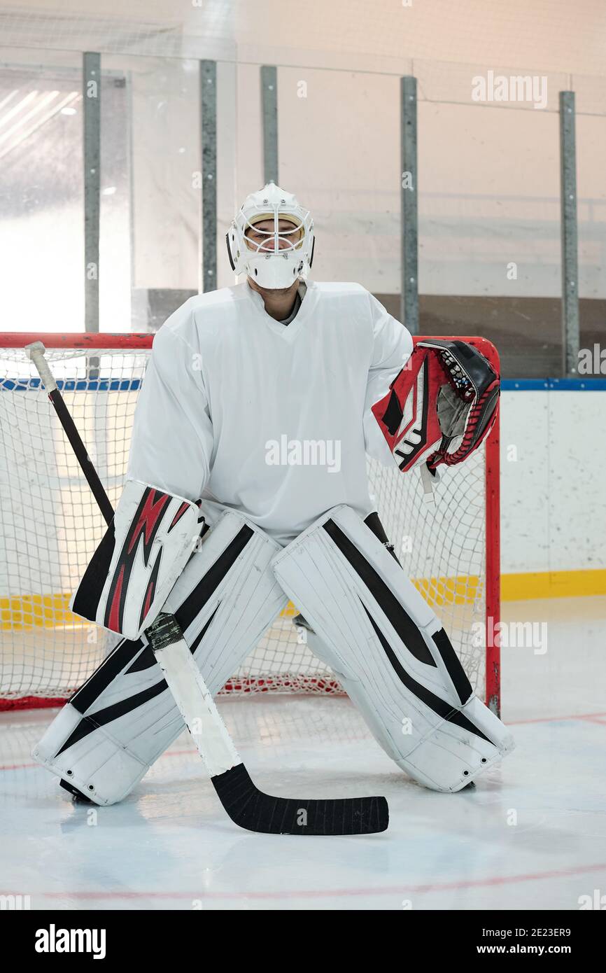 Zeitgemäßer Hockeyspieler in Sportuniform, Schutzhelm und Handschuhe halten Stock, während auf der Eisbahn gegen Netz stehen und auf Puck warten Stockfoto