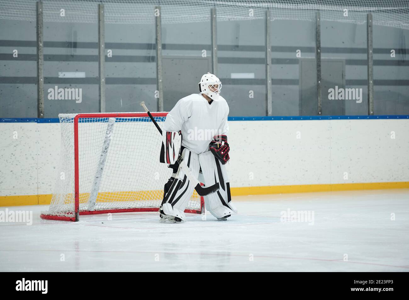 Hockeyspieler in weißer Sportuniform, Schutzhelm, Handschuhe und Schlittschuhe halten Stock, während auf der Eisbahn vor dem Netz stehen und warten auf Puck Stockfoto