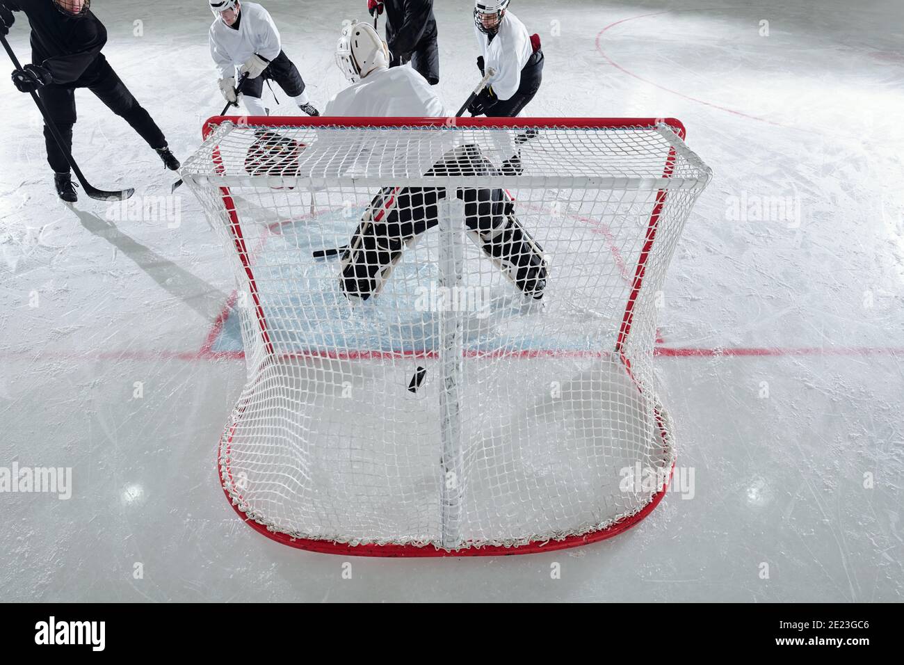 Rückansicht des Eishockeyspielers in Sportuniform und schützend Helm steht im Netz vor der Gruppe von Rivals angreifenden Puck während des Spiels Stockfoto
