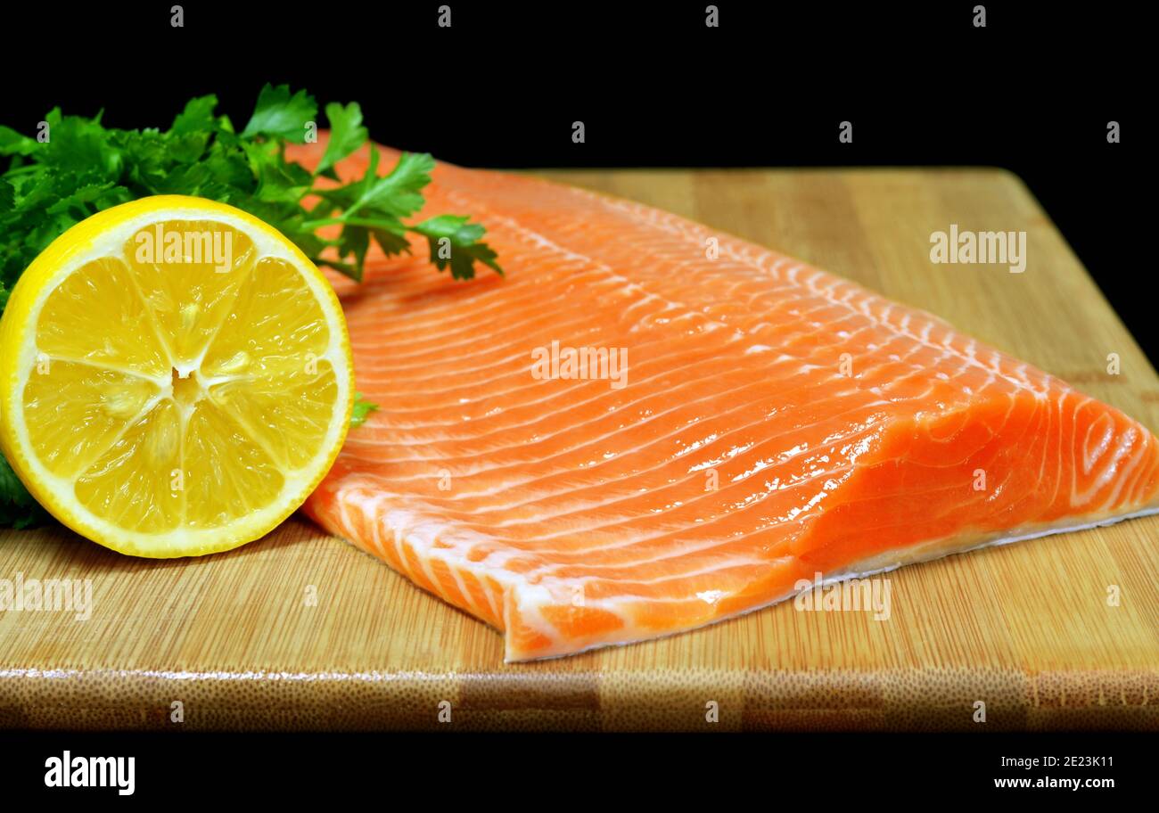 Rohes Lachsfischfilet mit Zitrone und frischen Kräutern Holzschneidebrett auf schwarzem Hintergrund Stockfoto