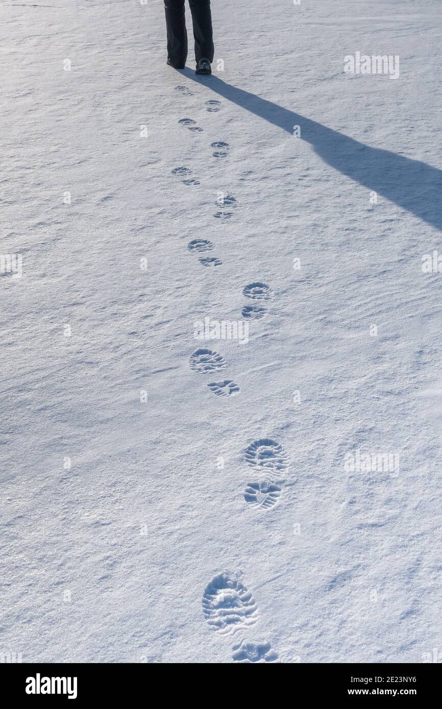 Eine Kette von klaren frischen Fußabdrücken von Stiefeln mit einem menschlichen Schatten auf dem Schnee an einem klaren sonnigen Wintertag. Stockfoto