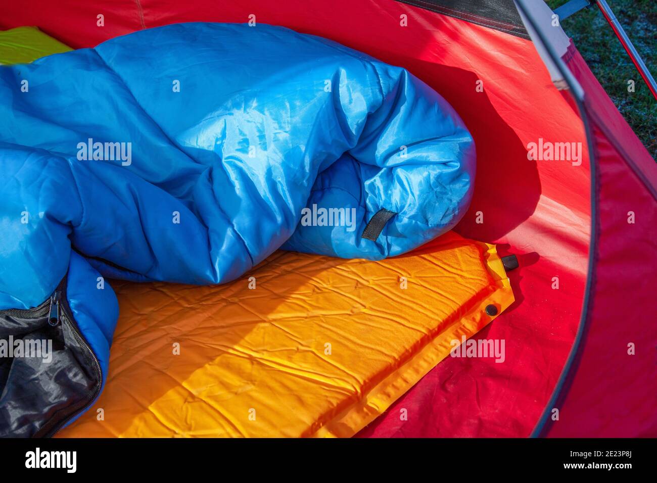 Das Innere eines roten Zeltes mit einem blauen Schlaf Tasche und eine orange selbstaufblasende Blow-up Matratzenauflage für unter Sein Schlafsack Stockfoto