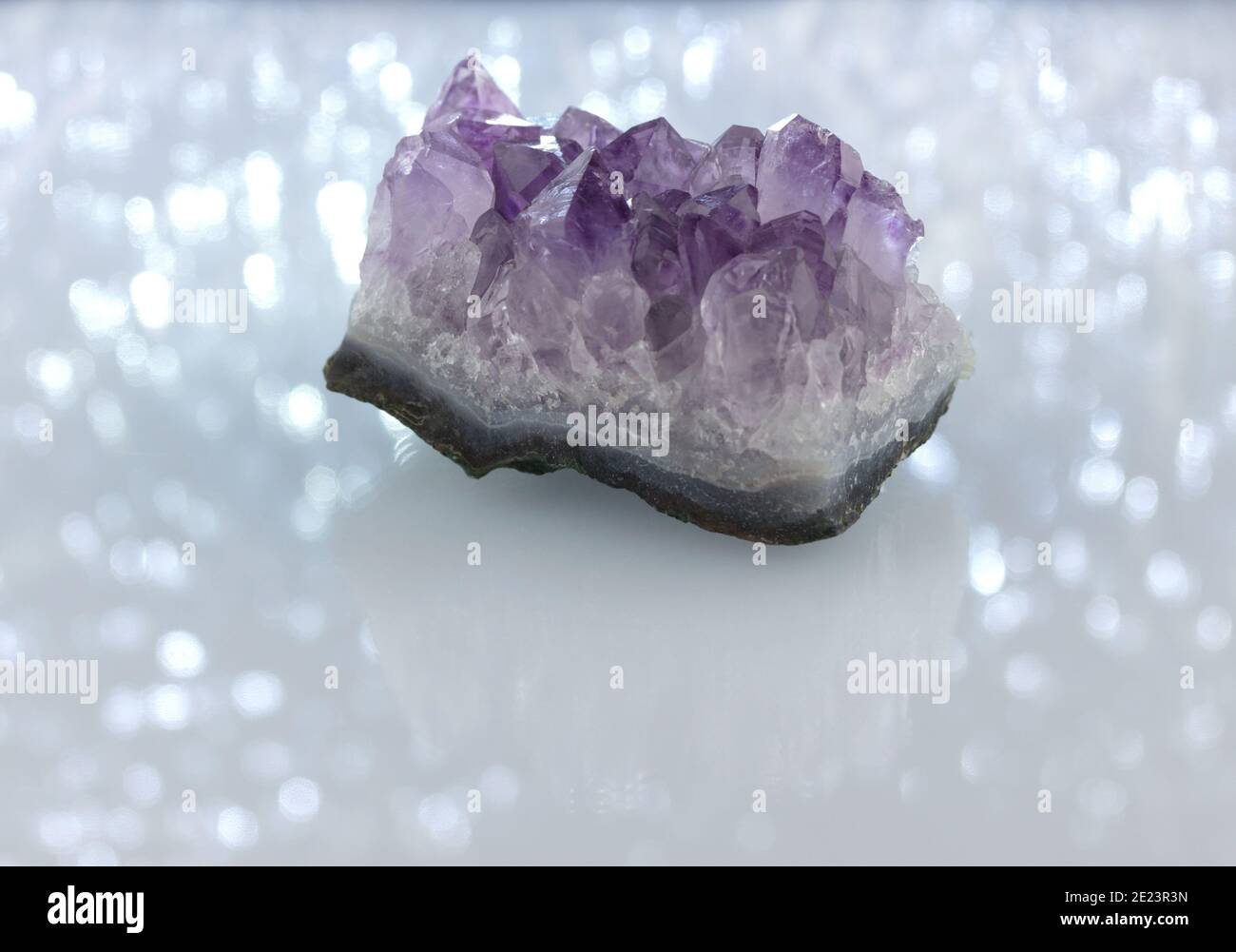 Ein rohes Amethyst-Kristallcluster, mineralisches Exemplar auf einem weißen funkelnden, schimmernden Hintergrund mit Reflexions- und Kopierraum Stockfoto
