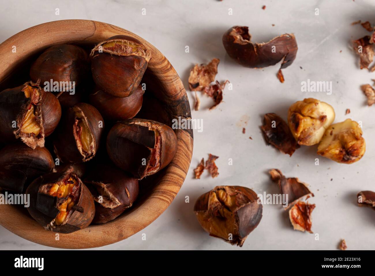 Eine Holzschale aus hausgemachten, im Ofen gerösteten Kastanien mit Muscheln und Schalen auf der Marmorplatte verstreut. Ein traditioneller Winter-, Herbst-Snack mit Stockfoto