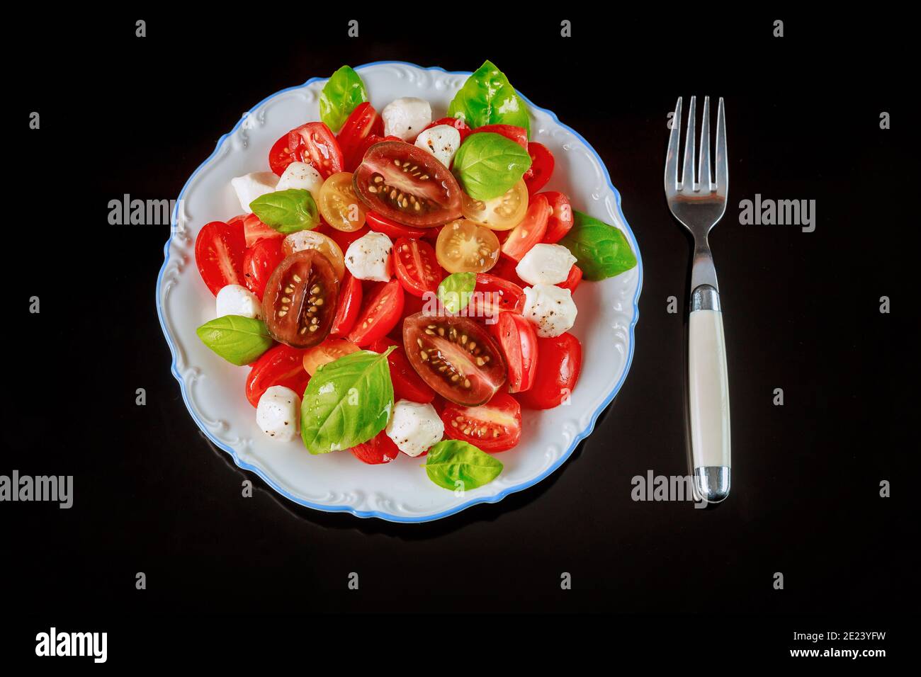 Kirschtomate mit Mozzarella-Käse auf weißem Teller mit Gabel. Nahaufnahme. Stockfoto
