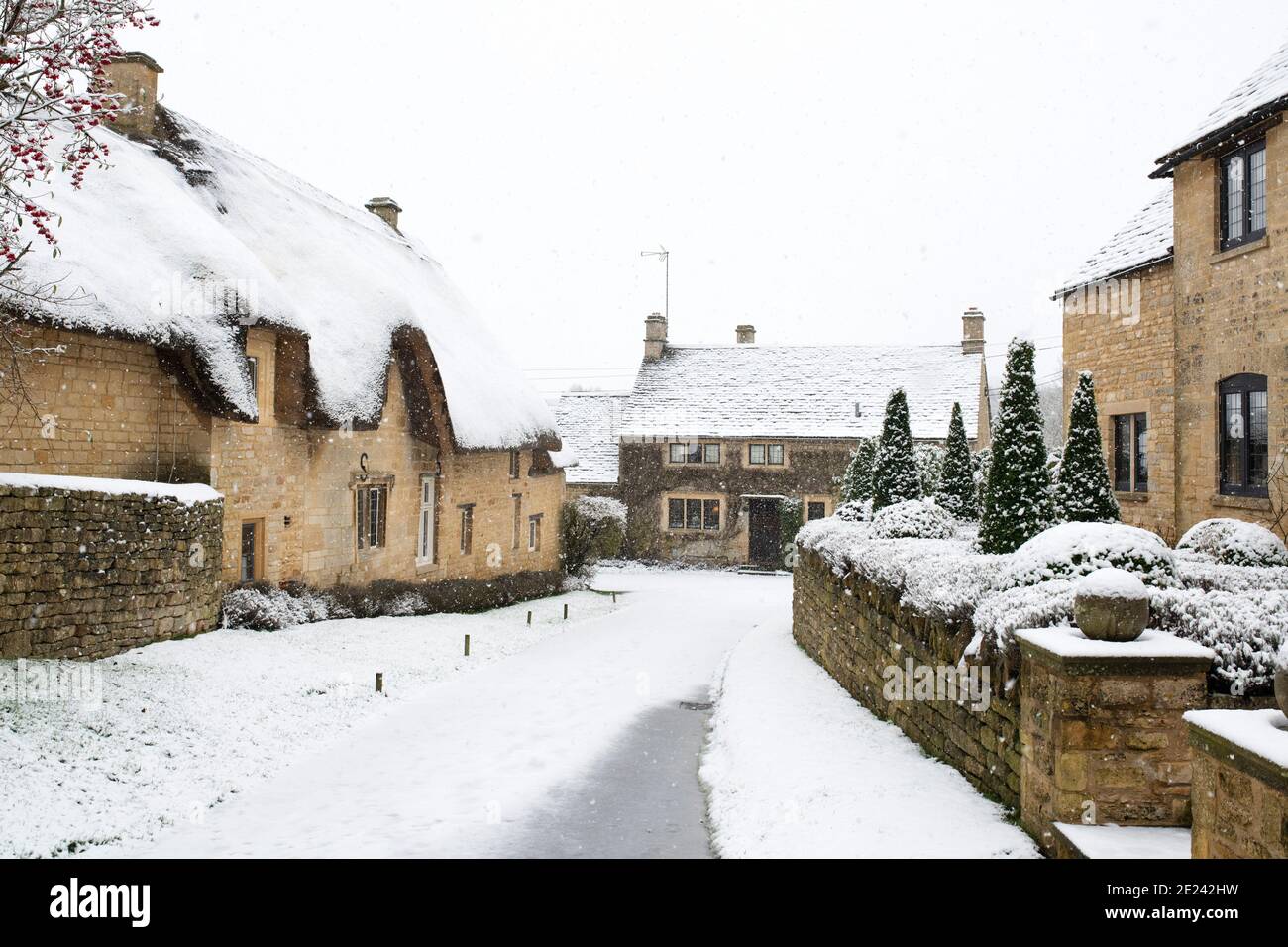 Cotswold Stein Reetgedeckten Hütte und Häuser entlang einer Straße im Schnee zu Weihnachten. Taynton, Cotswolds, Oxfordshire, England Stockfoto
