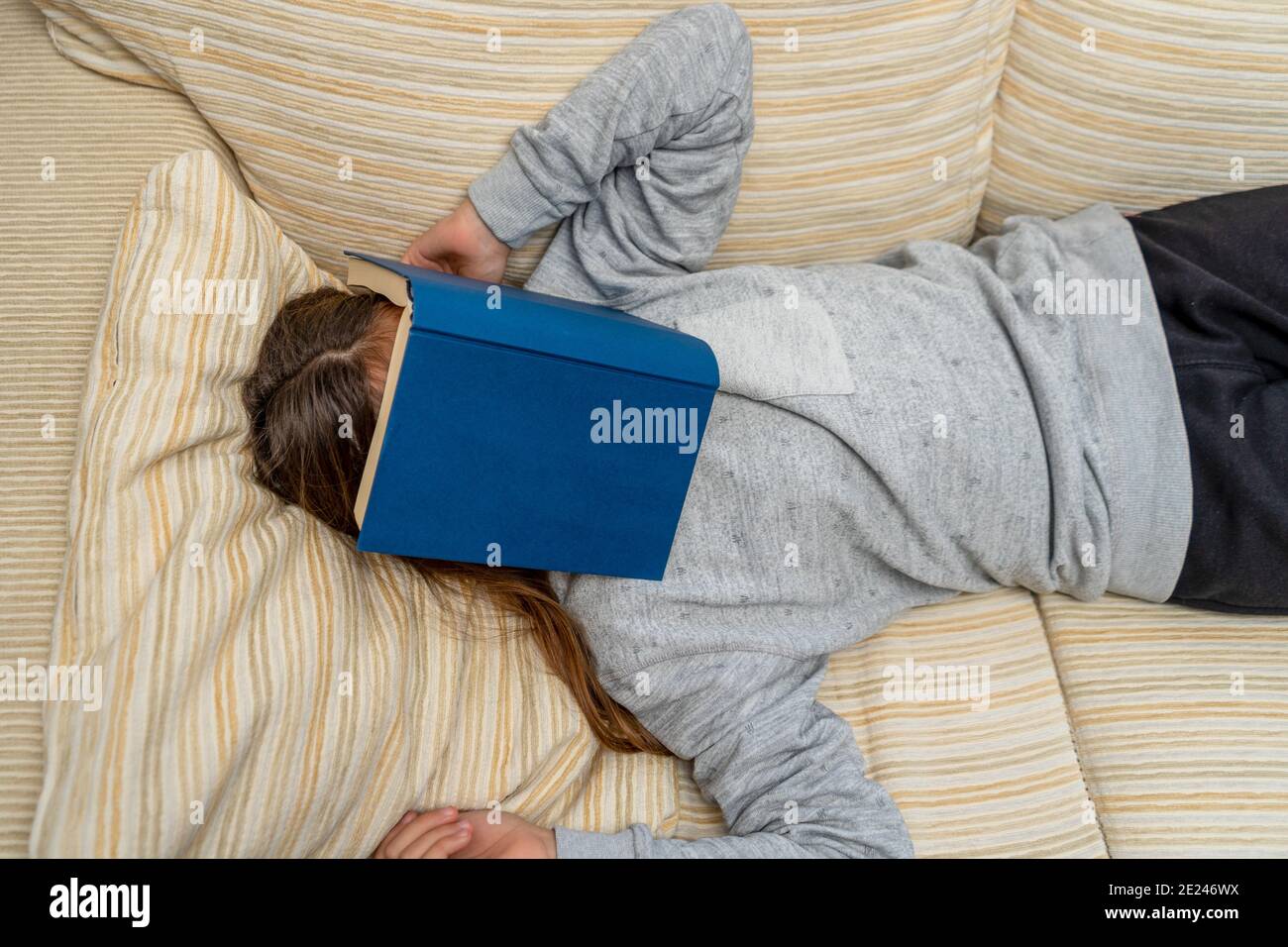 Nettes kleines Mädchen, das mit einem Buch nippt, das sie gerade auf dem Sofa in ihrem Wohnzimmer gelesen hat. Selektiver Fokus. Rest-Konzept. Stockfoto