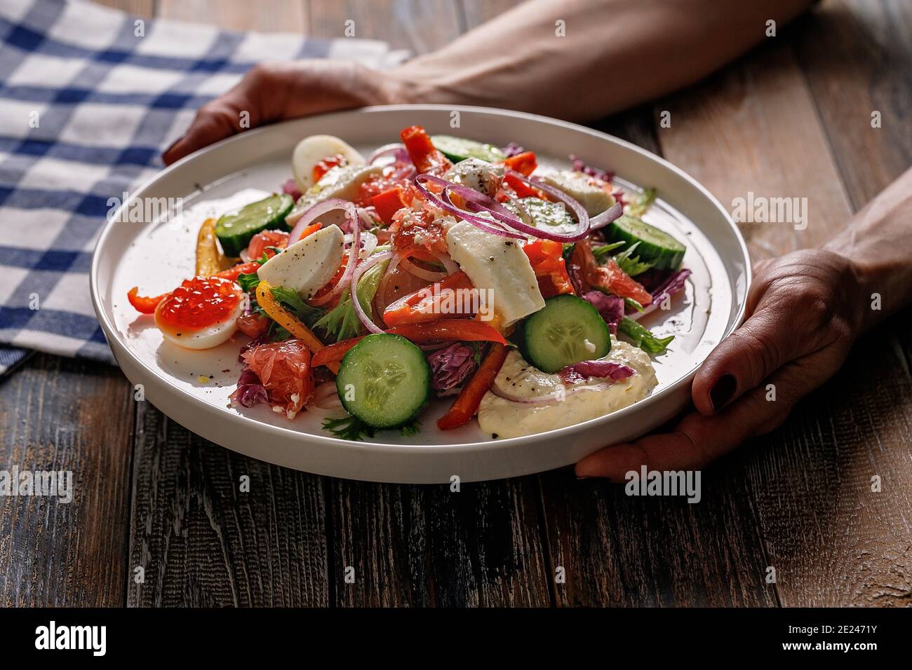 Weibliche Hände halten einen Teller mit einem Salat aus Gemüse und leicht gesalzenem Fisch. Leckere und gesunde Lebensmittel. Mittelmeer oder Keto-Diät. Holzhintergrund Stockfoto