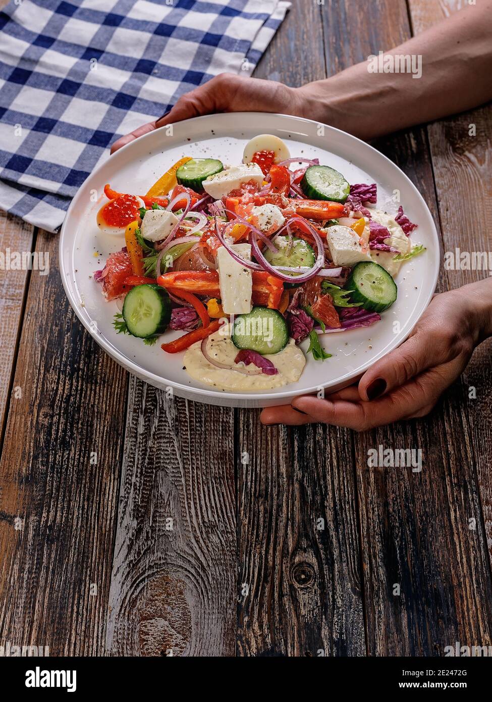 Weibliche Hände halten einen Teller mit einem Salat aus Gemüse und leicht gesalzenem Fisch. Leckere und gesunde Lebensmittel. Mittelmeer oder Keto-Diät. Holzhintergrund. Stockfoto