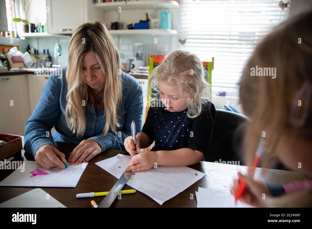 Ein dreijähriges Kind und ihre Mutter, die während der Covid-Pandemie gemeinsam Schularbeiten machen, zu Hause in der Küche Stockfoto