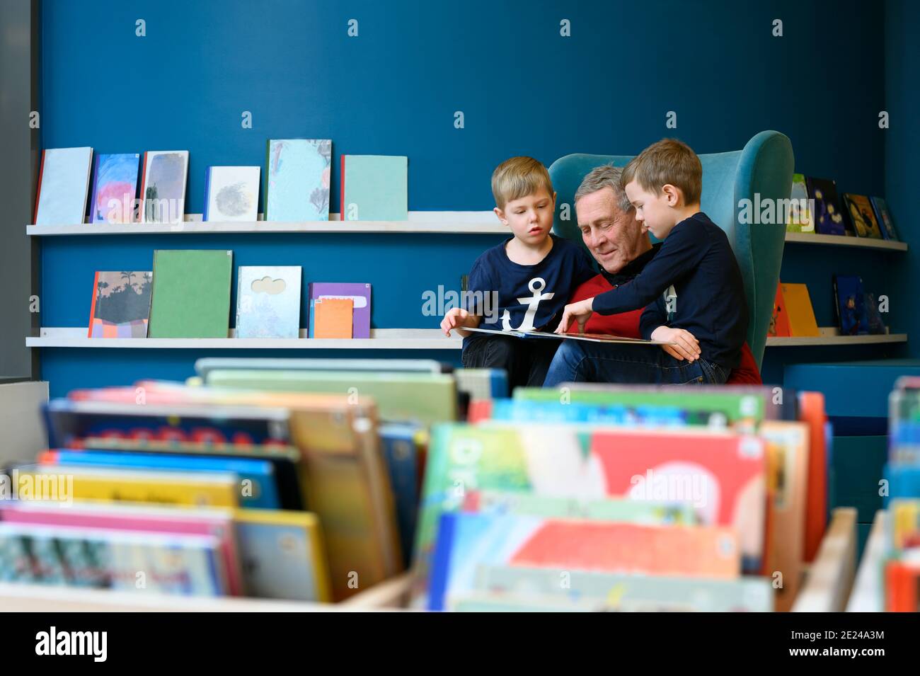 Großvater liest Buch zu Enkeln in der Bibliothek Stockfoto