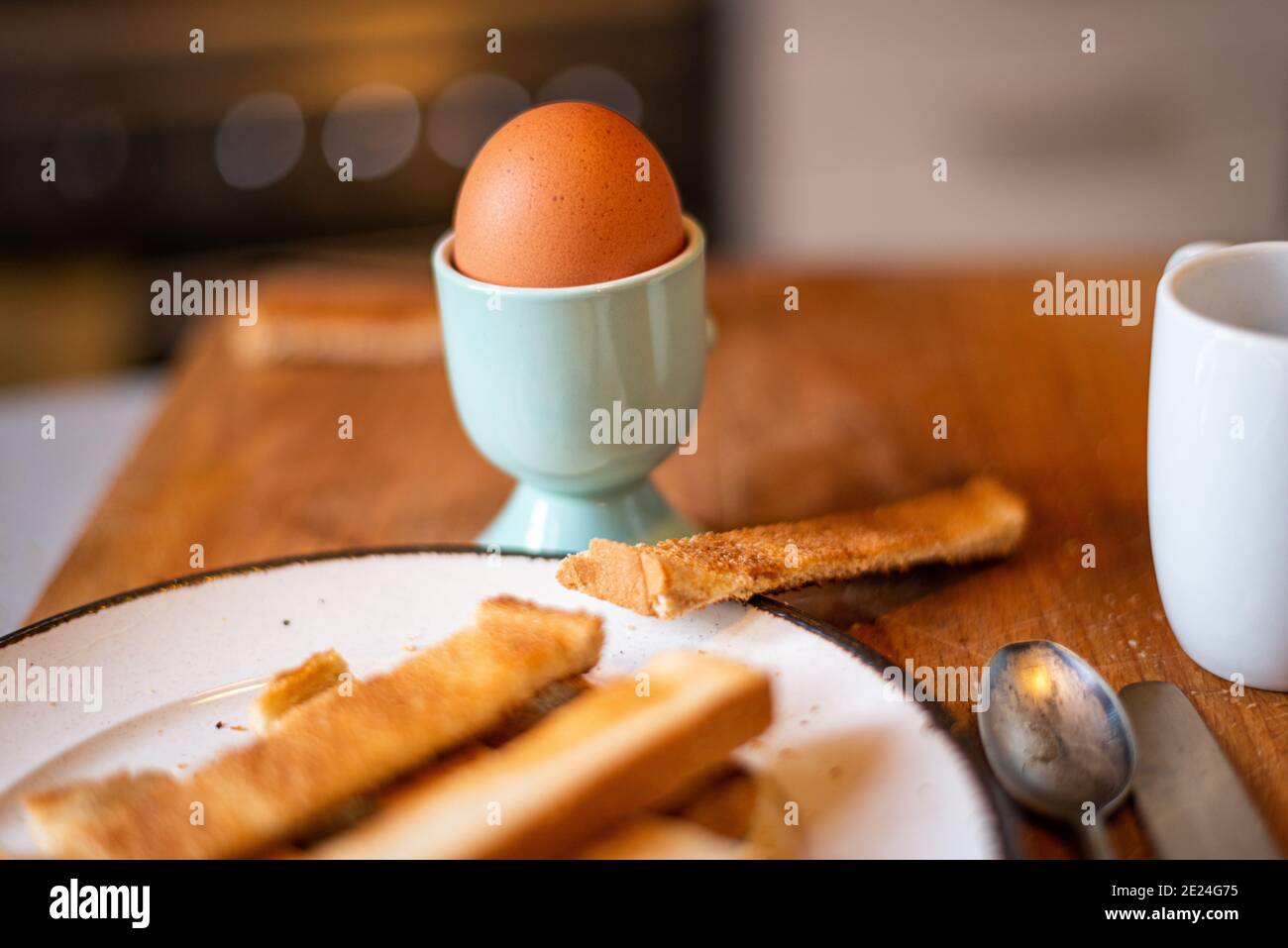 Weich gekochtes Ei in Eierbecher mit geröstetem Brot Soldaten, flache Tiefe des Feldes. Mit Kaffeetasse im Boden. Stockfoto