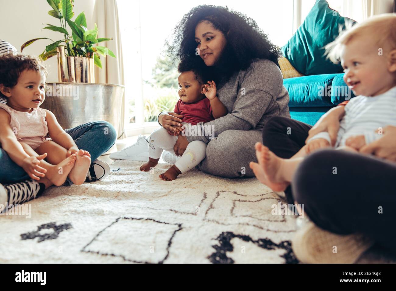 Mütter und ihre Kinder zusammen. Frauen mit ihren Babys sitzen zu Hause auf dem Boden. Stockfoto