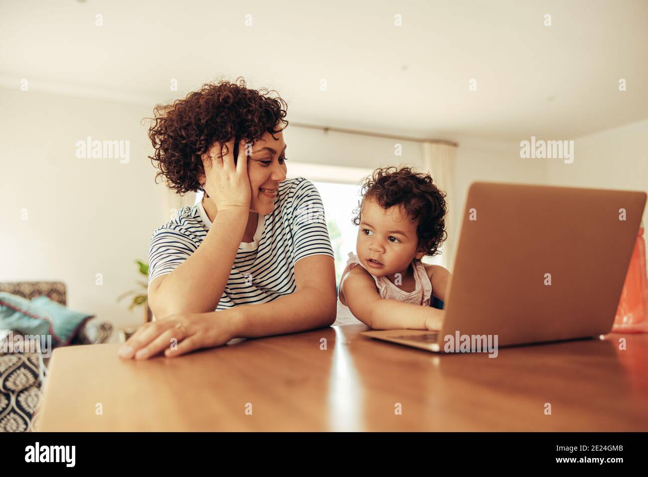 Frau sprechen Pause von der Arbeit und beobachten ihr Baby mit Laptop. Mutter und Kind sitzen am Tisch mit einem Laptop. Stockfoto