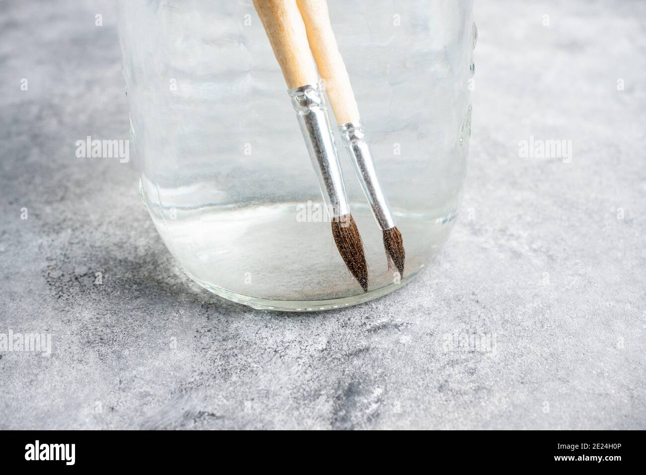 Künstlerische Pinsel in einem Glas mit Wasser auf dem grauen rustikalen Hintergrund. Interpreten-Tools. Selektiver Fokus. Stockfoto