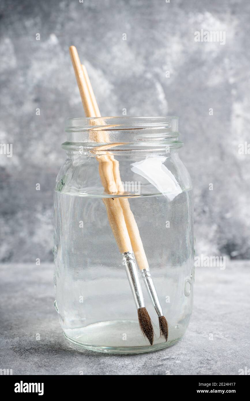 Künstlerische Pinsel in einem Glas mit Wasser auf dem grauen rustikalen Hintergrund. Interpreten-Tools. Selektiver Fokus. Stockfoto