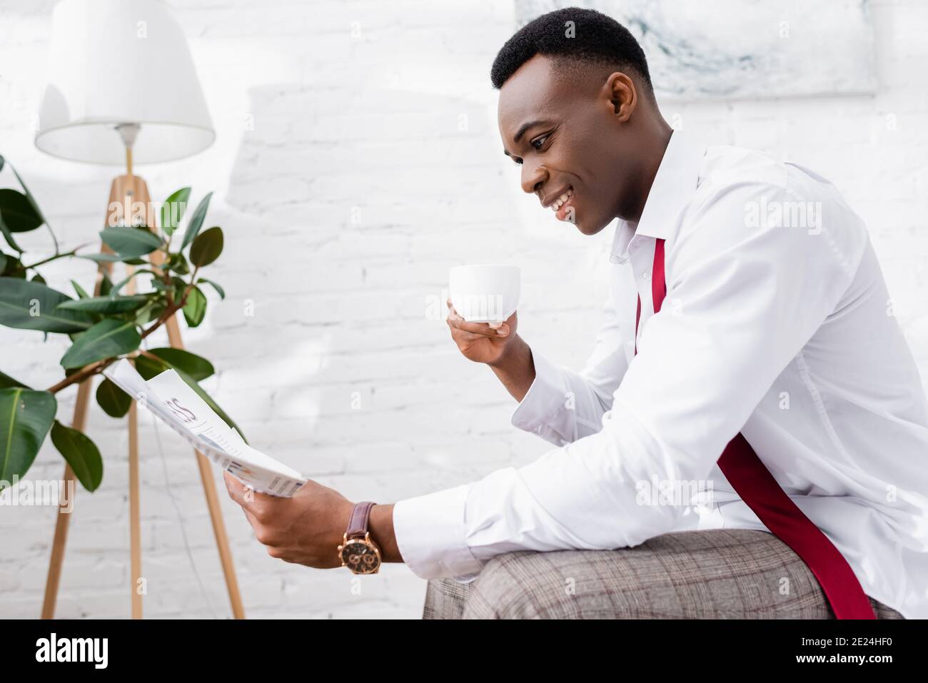 Lächelnder afroamerikanischer Geschäftsmann mit einer Tasse Kaffee beim Lesen der Zeitung Zu Hause Stockfoto