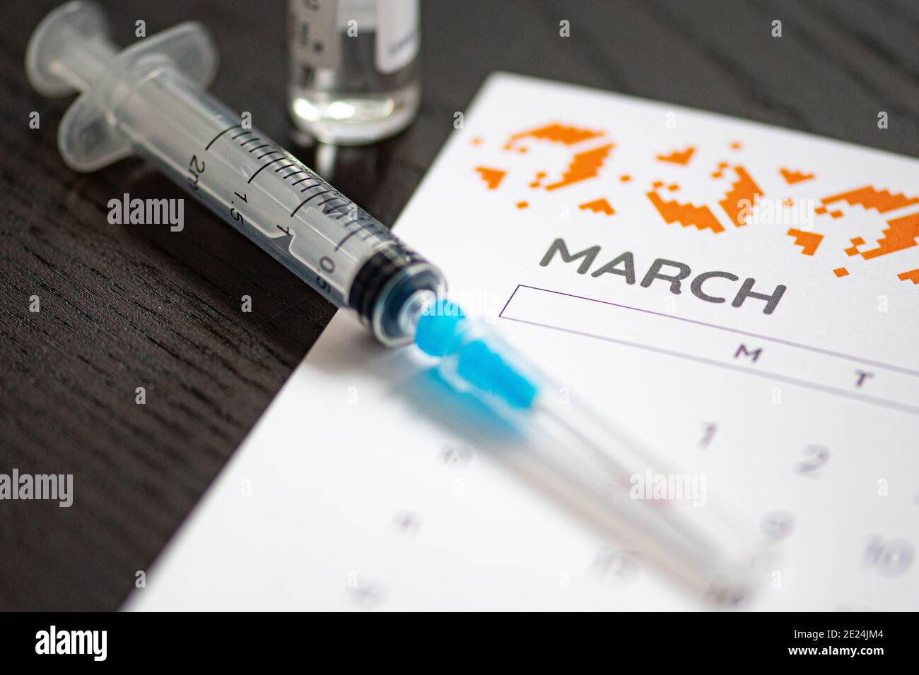 Nahaufnahme einer medizinischen Spritze auf einem März-Kalender mit einem Impfstofffläschchen im Hintergrund platziert, symbolisiert geplante Impfung, Gesundheitsplanung Stockfoto