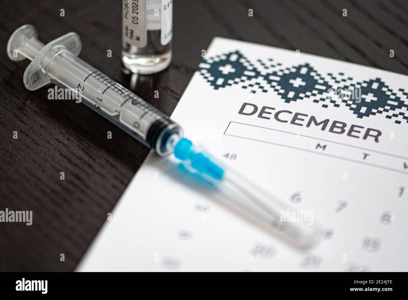 Nahaufnahme einer medizinischen Spritze auf einem Dezemberkalender mit einer Impfstoffflasche im Hintergrund, die die geplante Impfung symbolisiert Stockfoto