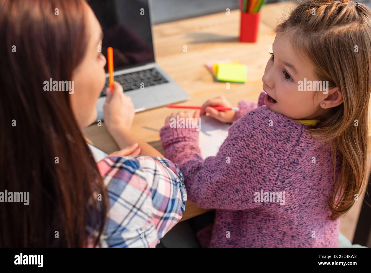 Aufgeregt Tochter mit offenem Mund Blick auf Mutter mit verschwommen Laptop im Vordergrund Stockfoto
