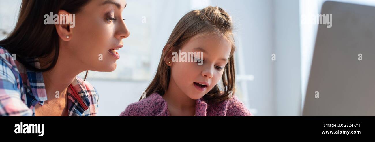 Mutter und Tochter schauen zu Hause mit verschwommenem Laptop im Vordergrund, Banner Stockfoto
