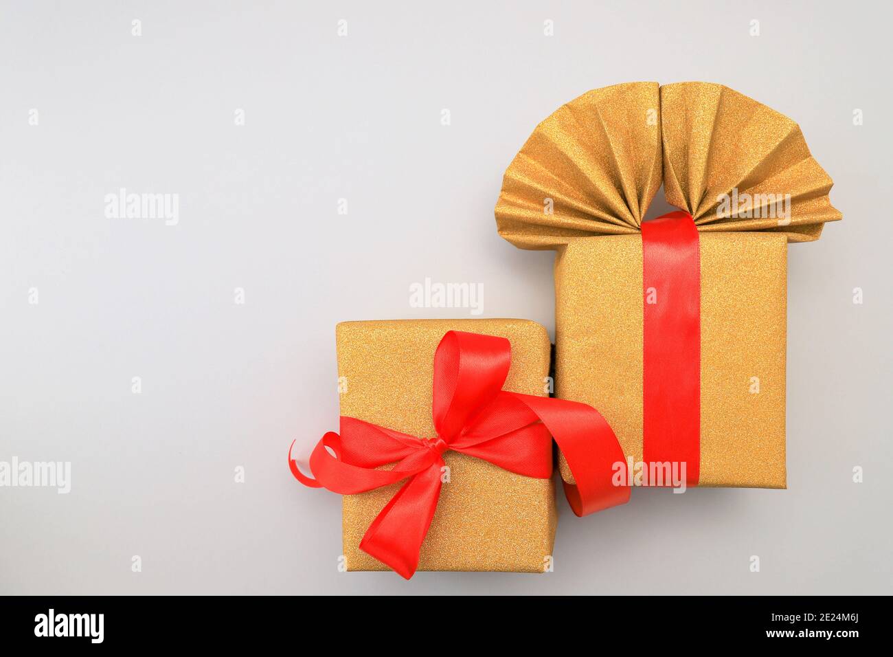 Goldene, gelbe Geschenkbox mit einer leuchtend roten Schleife auf grauem Hintergrund. Geburtstag, Festgeschenk. In den Farben 2021 Illuminating und Ultimate Grey. Stockfoto