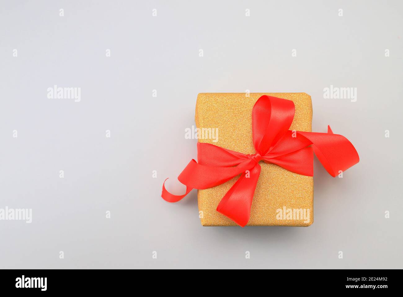 Goldene, gelbe Geschenkbox mit einer leuchtend roten Schleife auf grauem Hintergrund. Geburtstag, Festgeschenk. In den Farben 2021 Illuminating und Ultimate Grey. Stockfoto