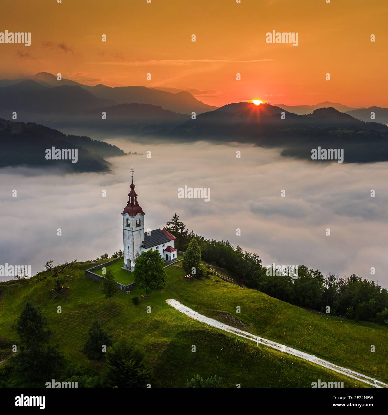 Šebrelje, Slowenien - Luftdrohnenansicht der wunderschönen Kirche des Hl. Ivan (Sv. Ivan Cerkev) bei Sonnenaufgang mit riesigen Morgennebel unten das Tal Stockfoto