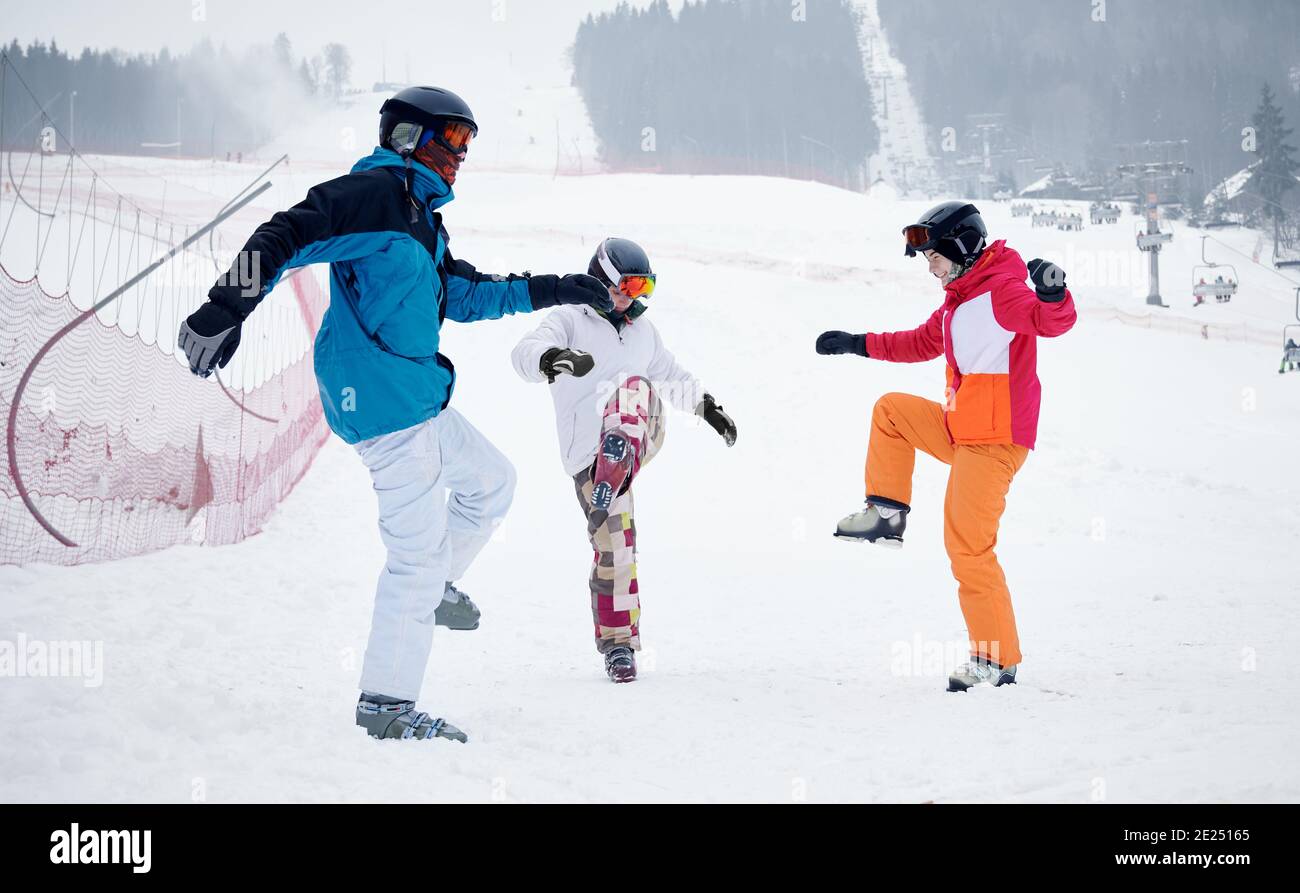 Eine Gruppe von Freunden, die lebhafte Skianzüge tragen, wärmen sich im Winter vor dem Skifahren von der Piste in den Bergen auf. Arbeiten auf Schnee, Spaß zusammen haben. Konzept des aktiven Lebensstils, Wintersport-Aktivitäten Stockfoto