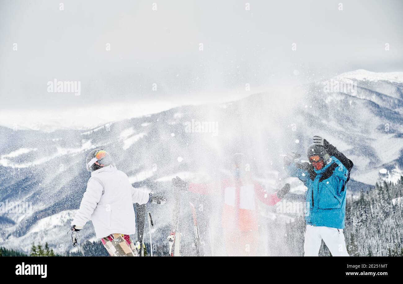 Freunde Skifahrer in Skianzügen werfen frischen Pulverschnee hoch in die Luft. Zwei Männer und Frauen, die Spaß auf verschneiten Hügel mit schönen Bergen im Hintergrund. Konzept der Winterunterhaltung, Freundschaft. Stockfoto