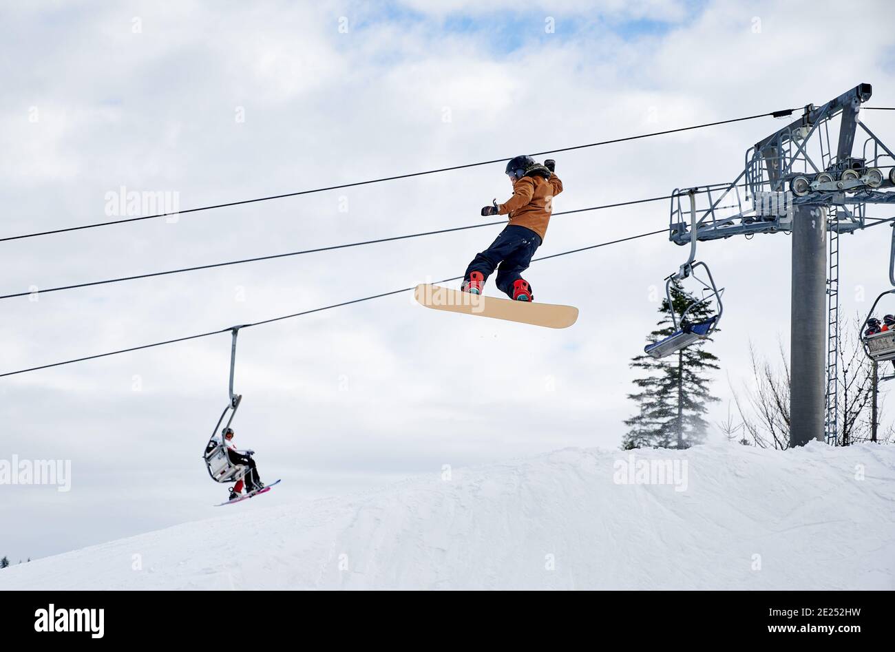 Snowboarder macht Tricks in den Bergen. Boy fliegen hoch mit Snowboard gegen Skilift und bewölkten Himmel. Low-Angle-Ansicht. Konzept des Wintersports, Extremsport im Skigebiet Stockfoto