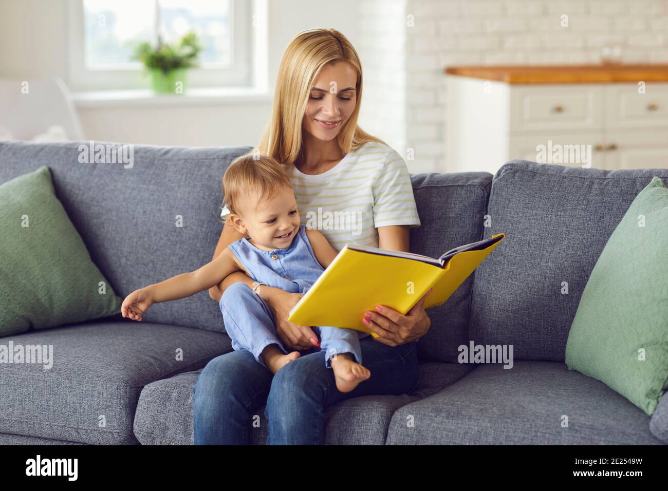 Mutter sitzt mit ihrem Baby auf den Knien und liest Buch Oder sich zu Hause ein Album mit Bildern anzusehen Stockfoto