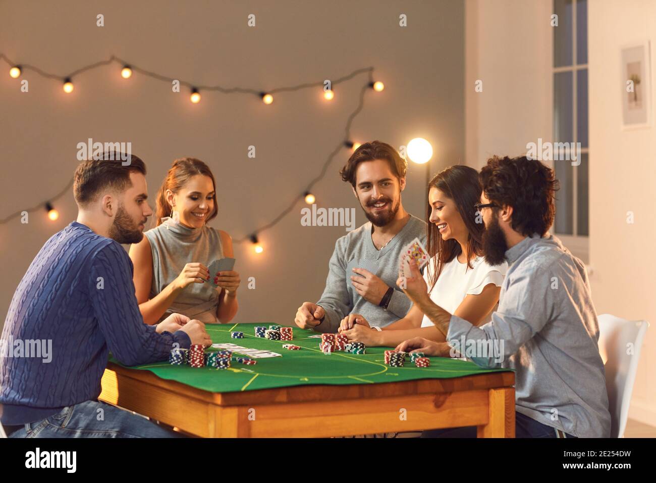 Fröhliche freundliche Gesellschaft von Männern und Frauen, die an einem Pokertisch sitzen und das Spiel genießen. Stockfoto