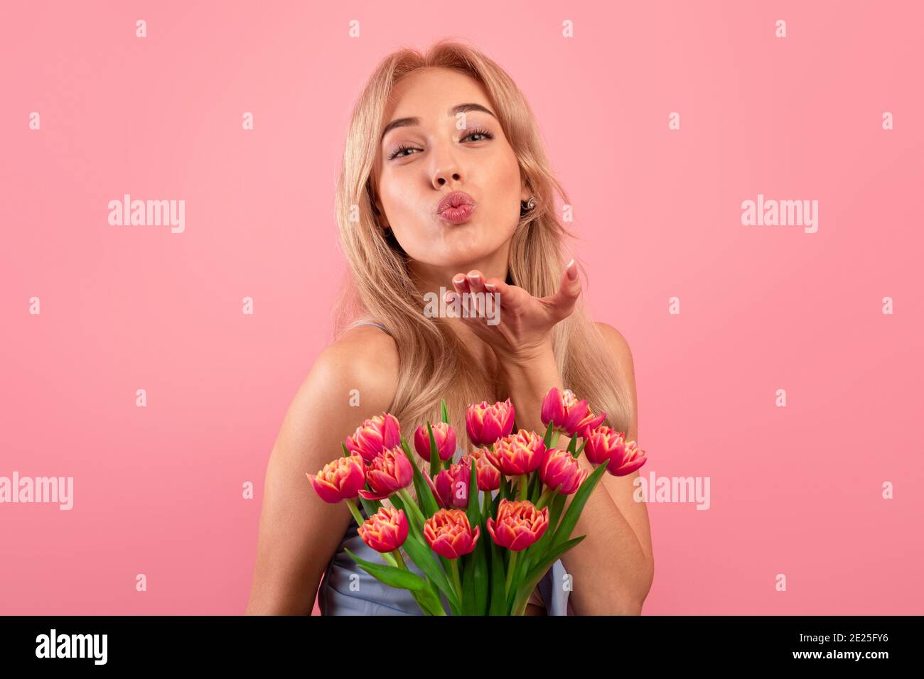 Schöne junge Dame mit Blumenstrauß weht Luft Kuss auf Kamera über rosa Studio Hintergrund. Frauentag Stockfoto