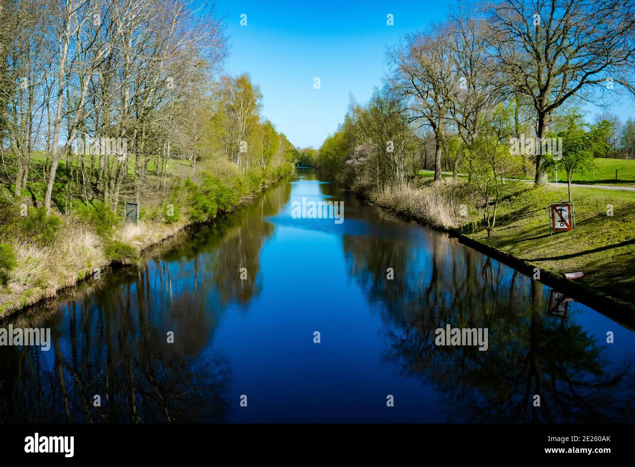 Schöne Aufnahme von Bäumen und Sträuchern, die sich auf dem Wasser spiegeln Oberfläche von Ems-Jade Kanal Stockfoto