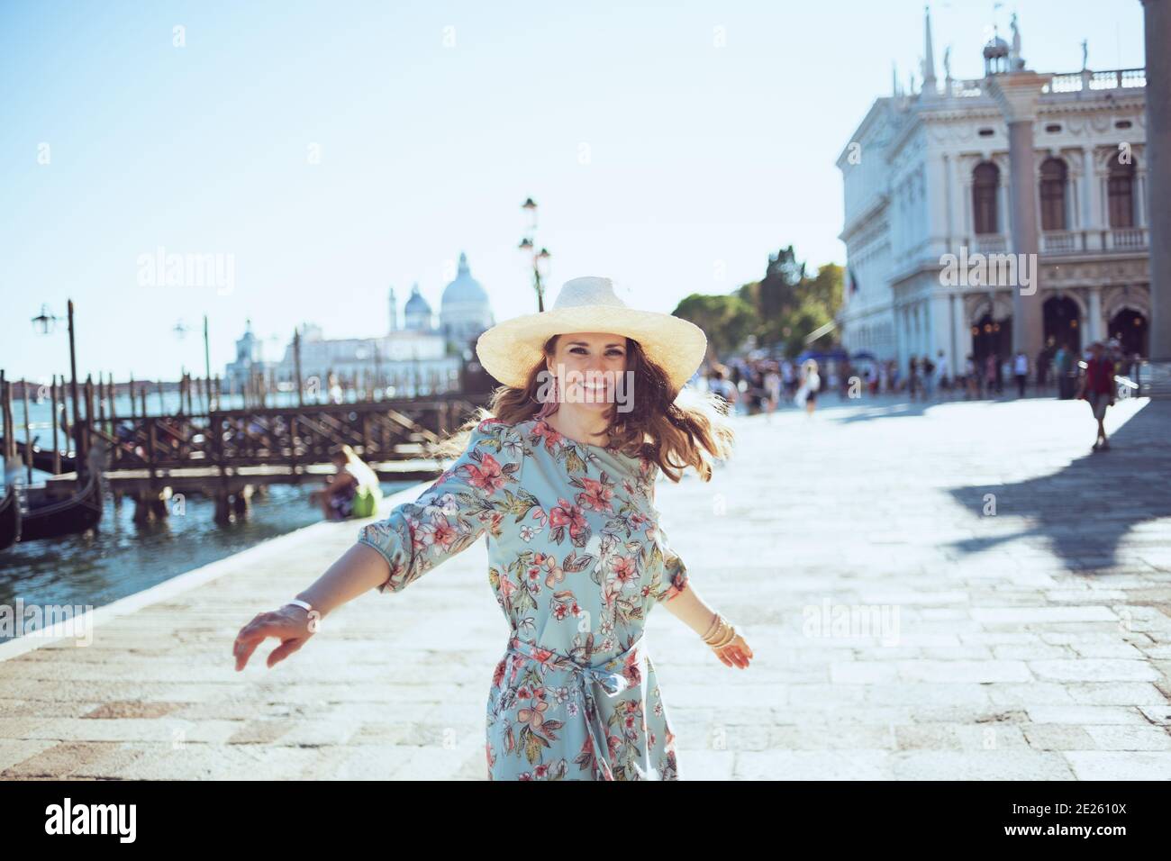 Glückliche moderne Reisende Frau mittleren Alters in floralem Kleid mit Hut Sightseeing am Ufer in Venedig, Italien. Stockfoto