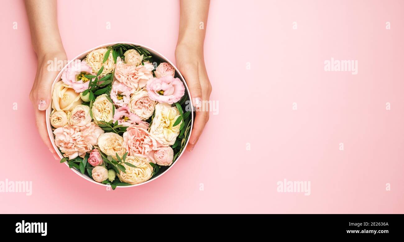 Florist hält einen Hut runde Box mit floralen Komposition auf einem rosa Hintergrund mit Copy Space. Geschenkbox für 8. März, Valentinstag, Muttertag Stockfoto