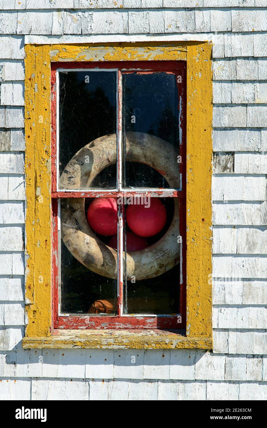 Ein gelb gerahmtes Fenster in einem verwitterten weißen Fischschuppen Fenster in der Nähe von Blue Rocks, Nova Scotia zeigt einen Rettungsring und Bojen Stockfoto