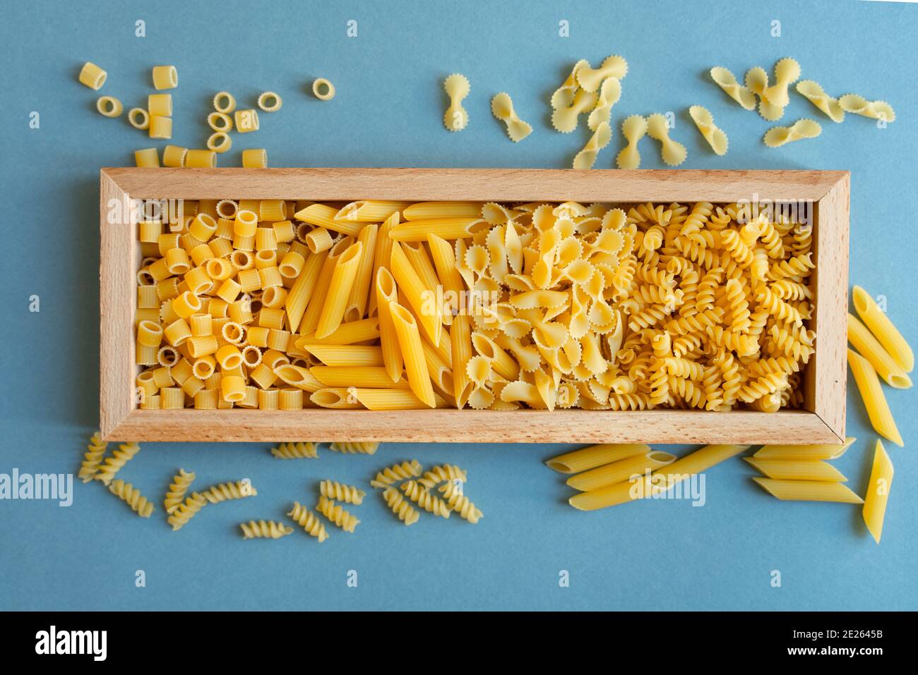 penne, farfalle tonde Schmetterling, Schnecke und Ditalini Art von Pasta auf hellblauem Hintergrund. Pasta in einer Holzkiste Teller. Abstrakt, Pasta. Draufsicht Pho Stockfoto