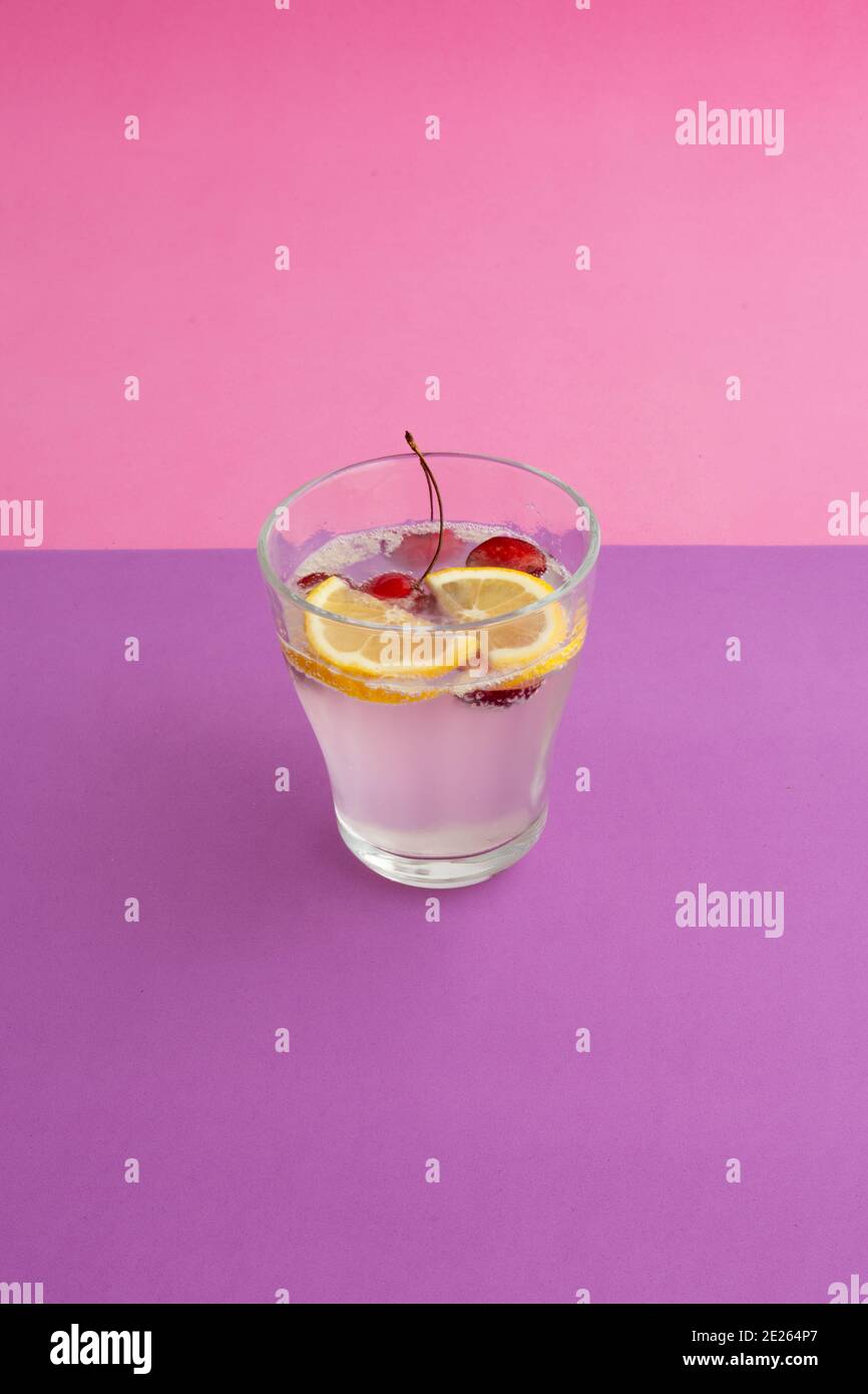 Ein Glas Sekt Cocktail mit Zitrone, Kirsche und Beere in Scheiben geschnitten. Alkoholfreie Getränke, Getränke. Lila strukturierte Hintergrund und rosa Hintergrund. Stockfoto