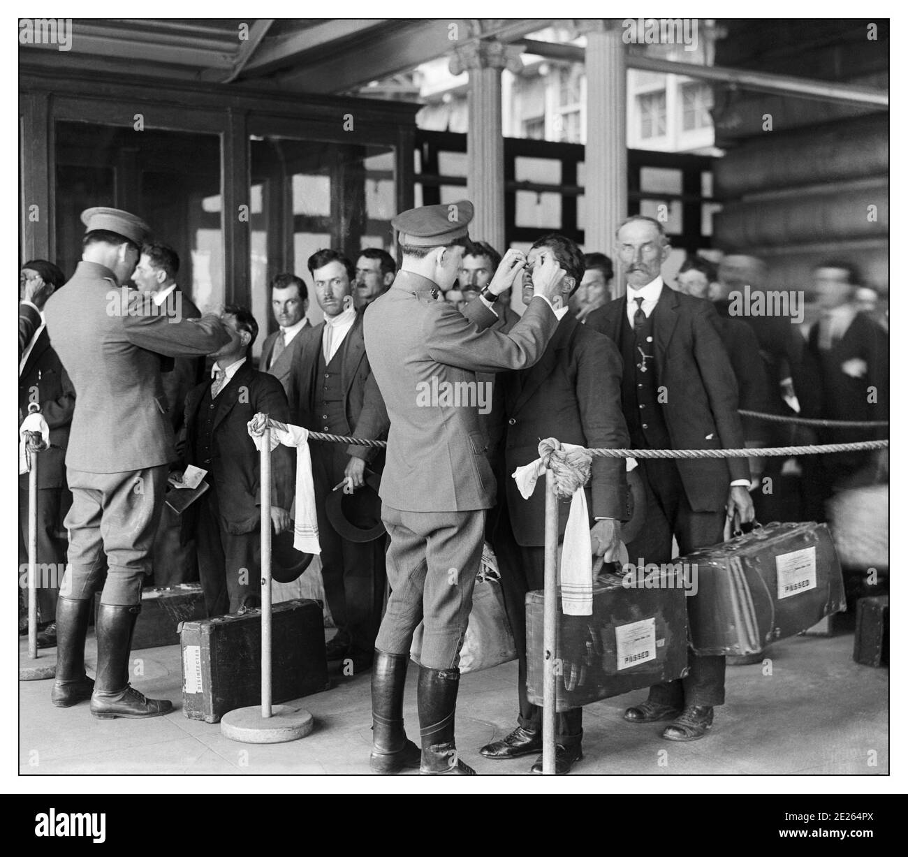 ELLIS ISLAND Vintage 1900 USA IMMIGRATION “Health Inspection of New Immigrants, Ellis Island, USA 1914 nach einer mühsamen Seereise, Immigranten, die auf Ellis Island ankommen, wurden mit Informationen aus ihrem Schiffsregister markiert; Sie warteten dann auf langen Warteschlangen für medizinische und rechtliche Inspektionen, um festzustellen, ob sie für die Einreise in die Vereinigten Staaten geeignet waren. Von 1900 bis 1914 – den Spitzenjahren des Ellis Island-Betriebs – kamen täglich durchschnittlich 1,900 Menschen durch die Einwanderungsstation. Stockfoto