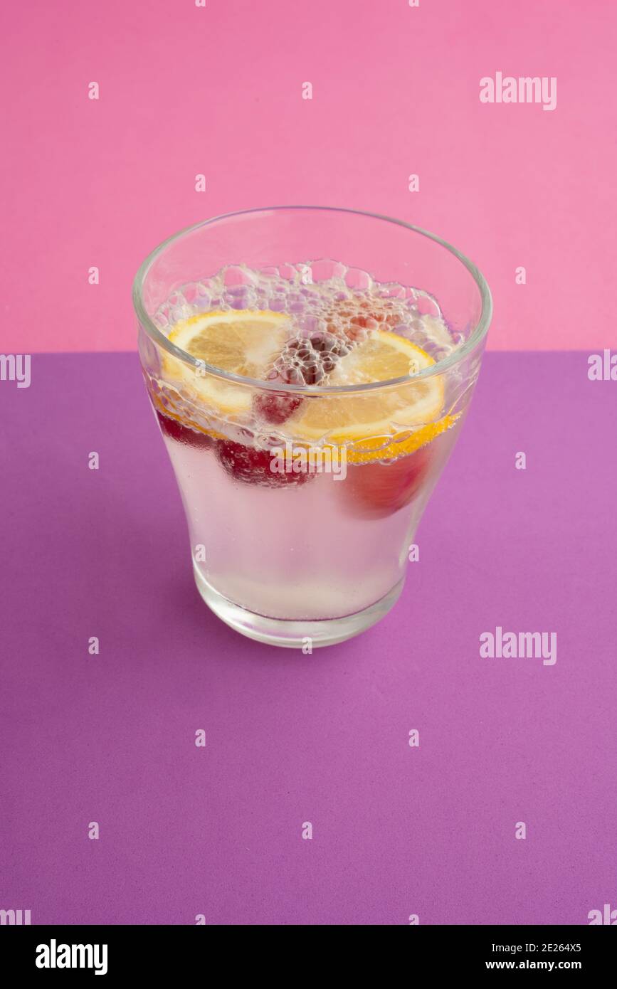 Ein Glas Sekt Cocktail mit Zitrone, Kirsche und Beere in Scheiben geschnitten. Alkoholfreie Getränke, Getränke. Lila strukturierte Hintergrund und rosa Hintergrund. Stockfoto