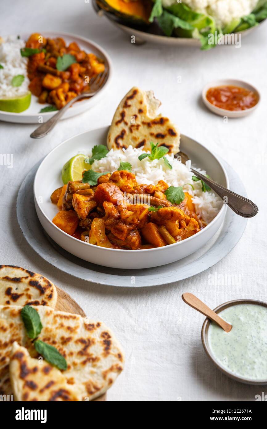 Blick von oben auf ein vegetarisches, veganes indisches Balti-Curry mit Blumenkohl und Kürbis, serviert mit Raita, Naan-Brot und Mango-Chutney und Basmati-Reis o Stockfoto