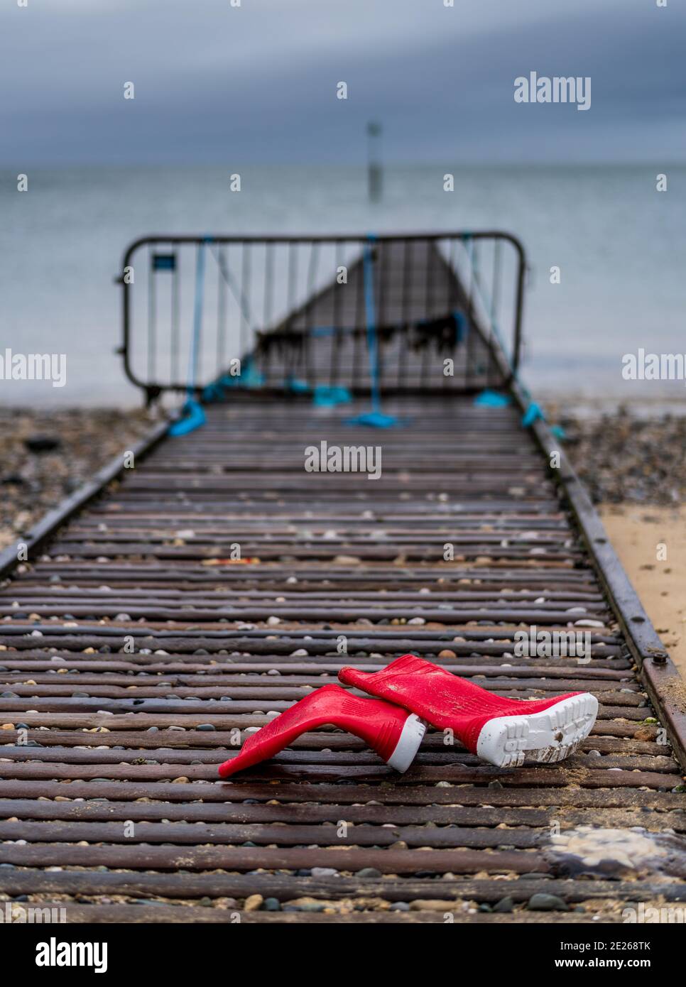 Verlorene Red Wellies am Strand - hinter roten wellington-Stiefeln auf einem Küstensteg am Strand zurückgelassen. Rote Stiefel. Rote Gummistiefel. Stockfoto